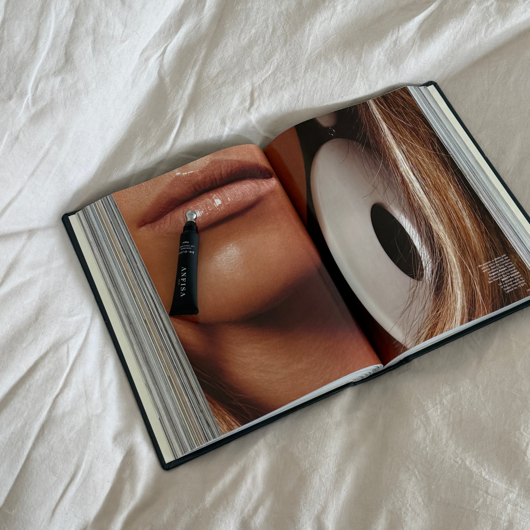 Open book showing a close-up of lips and an eye with a cosmetic product on a white fabric background
