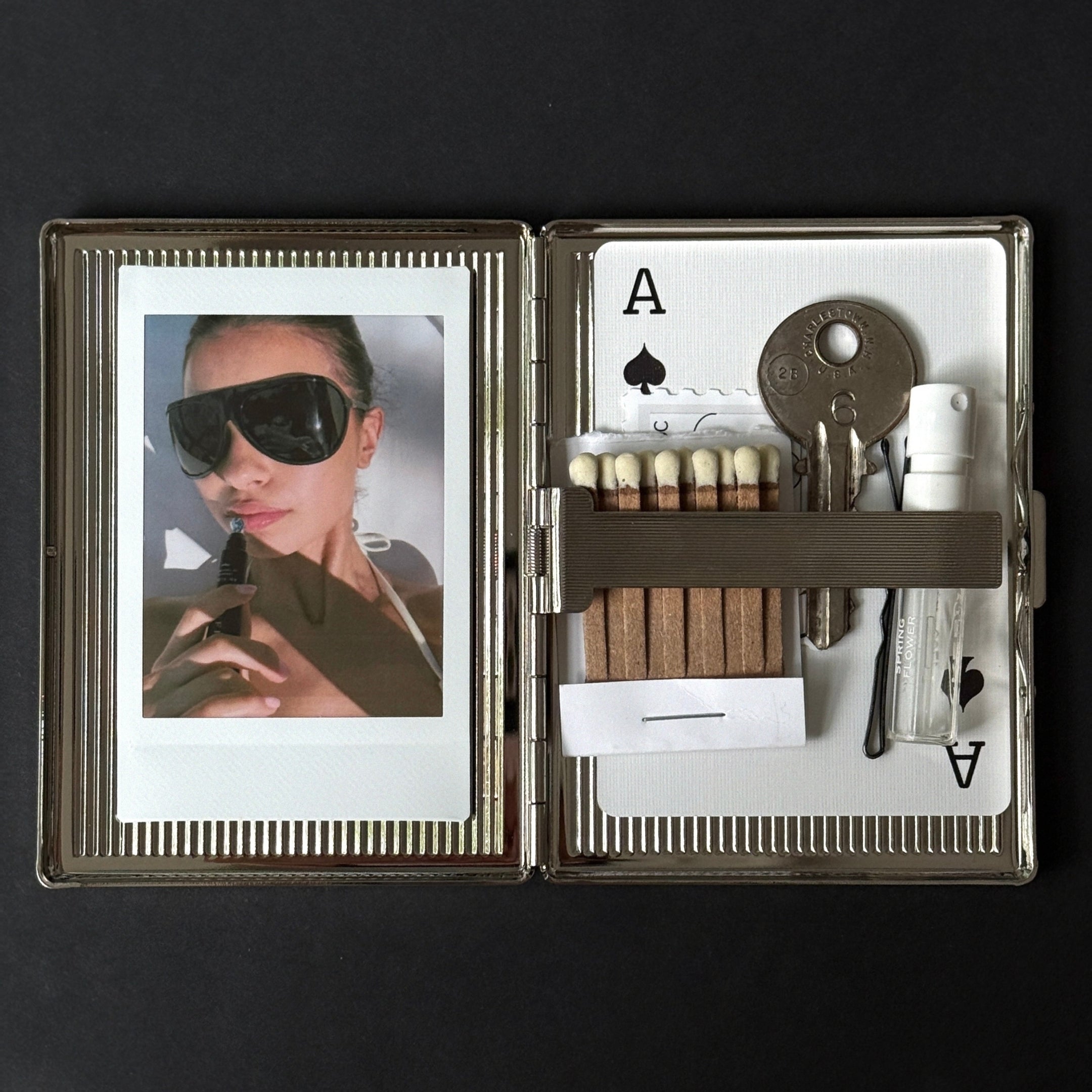 Open case with a photo of a woman, playing card symbols, and various items on a black background
